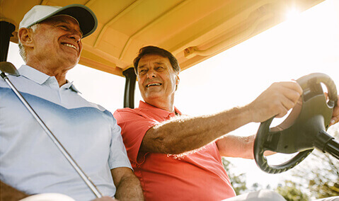 Two happy mature men riding in golf cart