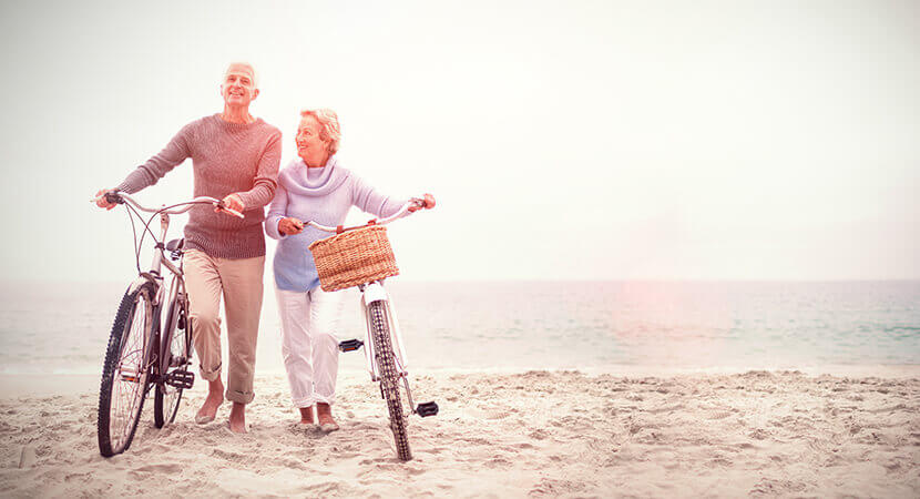 Mature couple walking bikes on beach